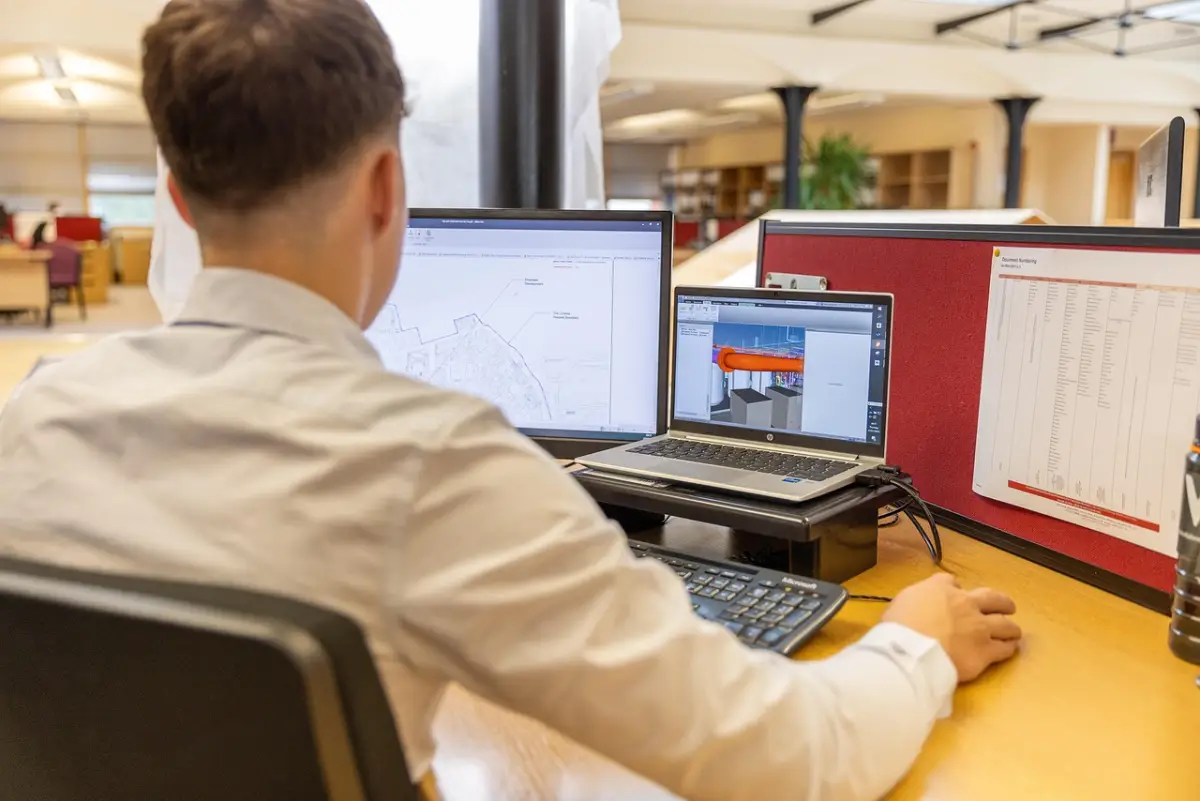 Engineer am Arbeitsplatz mit Laptop und mehreren Bildschirmen — Symbolbild für professionellen Business-Arbeitsplatz