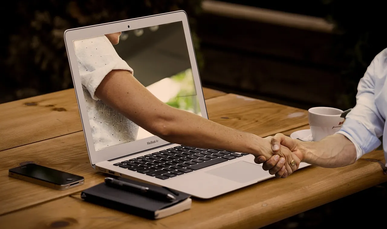 Handshake über Laptop am Besprechungstisch — Projektpartner starten IT-Integration mit klarer Anforderungsanalyse